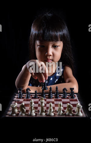 Kleine chinesische Asiatin spielt Schach in isolierten schwarzen Hintergrund Stockfoto