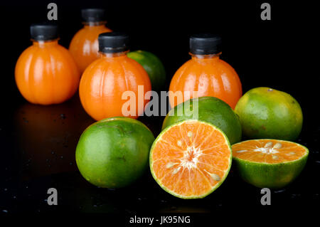 Grün orange Obst und Orangensaft in die Plastikflasche inmitten Studiobeleuchtung. Stockfoto