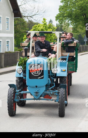 Junge Männer und Frauen im bayerischen Kostüme sitzen auf einem Anhänger, gezogen von einen alten Traktor, Ankunft in eine traditionelle kann Feier Stockfoto