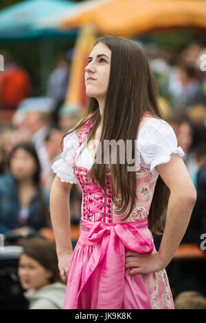 Junge Bayerin im traditionellen Dirndl Kleid mit Armen gestemmt nachschlagen während der Durchführung traditionellen Volkstanz Bandltanz rund um den Maibaum Stockfoto