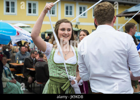 Junge Frau im traditionellen Dirndl Kleid und männlichen Partner halten Bänder während der Durchführung traditionellen Volkstanz Bandltanz rund um den Maibaum Stockfoto