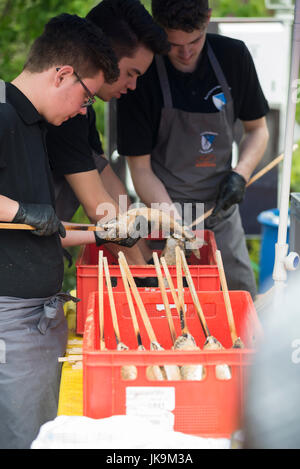 Panierter Fisch sind auf einem Holzstab von jungen Männern, zum Grillen als einheimische Spezialität in Bayern auf Mai Feier spucken Stockfoto