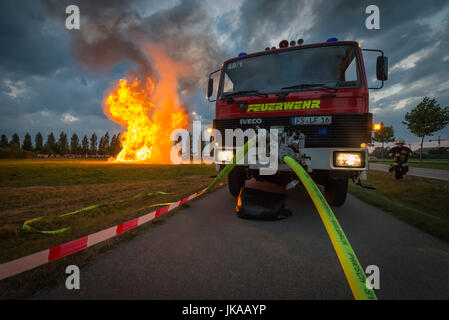 Fire-Fighter auf Feuerwehrauto spritzt Wasser gegen Funkenflug der Feuersäule bei Sonnenwende feiern und Sonnwendfeuer Stockfoto