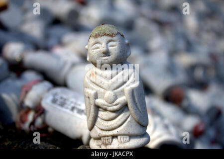 Eine kleine buddhistische Statue sitzt vor einen großen Haufen von ähnlichen Statuen. Stockfoto