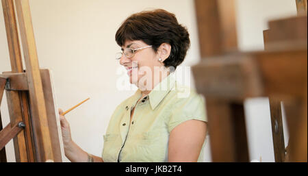 Ältere Menschen Gemälde für Hobby. Gruppe von aktiven Senioren an der Kunsthochschule. Porträt der glückliche alte Frau lächelnd und Pinsel halten. Stockfoto