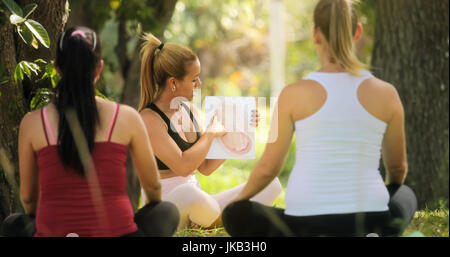 Schwangere Frauen, die pränatale Lektion im Park. Lehrer erklärt Wachstum des Babys im Bauch mit Bildern und Zeichnungen. Stockfoto