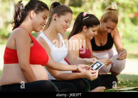 Schwangere Frauen, Gruppe von Müttern während der Schwangerschaft. Lektion im Stadtpark mit glücklich Freundinnen lächelnd und Blick auf Sonografie scannt. Stockfoto