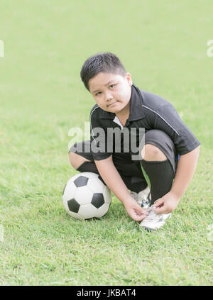 übergewichtige junge immer bereit für das Fußballspiel binden seine Schuhe, gesundes Konzept Stockfoto