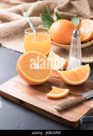 Frisch geschnittenen Orange auf Holzplatte und Orangensaft mit Sack und schwarzem Stein. Stockfoto