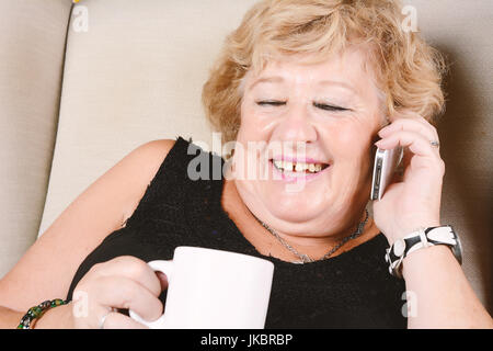 Porträt einer alten Frau am Telefon zu sprechen und auf Couch sitzen. Im Innenbereich. Stockfoto