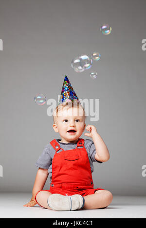 glückliches Baby junge mit Hut und Schaum Luftballons Geburtstag, Studio gedreht Stockfoto