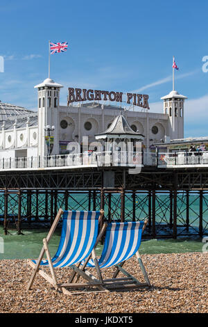 Zwei leere Liegestühle mit Blick auf Pier von Brighton an der Südküste von England. Stockfoto