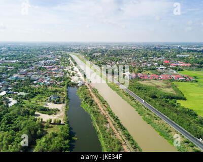 Luftaufnahme von Drohne: Bewässerungskanal mit Dorf auf Land, Thailand Stockfoto