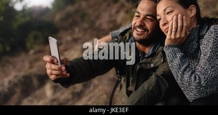 Horizontalen Schuss liebevollen jungen Paar auf Wanderung nehmen ein Selbstporträt mit Smartphone im Freien. Entspannte Wanderer-paar in den Urlaub nehmen Selfie mit cel