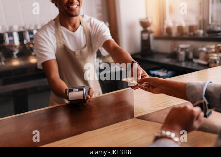 Schuss die Kreditkarte des Kunden, männliche Barista an Café-Kasse beschnitten. Kunden zahlen mit Kreditkarte im Coffee Shop. Stockfoto