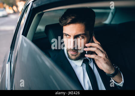 Geschäftsmann, telefonieren mit dem Handy und auf der Suche nach draußen vor dem Fenster beim Sitzen auf dem Rücksitz eines Taxis. Männliche Führungskraft Reisen von einem c Stockfoto