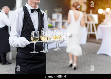 Mittelteil des professionellen Kellner in Uniform mit Wein während Buffet catering Party, Feier oder Hochzeit. Volle Gläser auf Tablett. Stockfoto