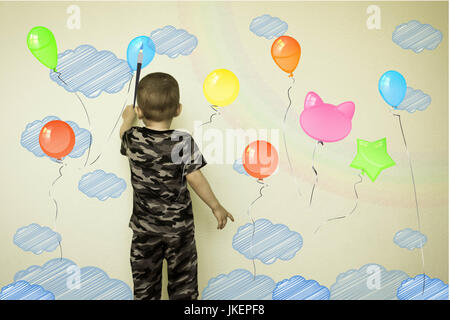 Konzept der Kreativität Kind. Der kleine Junge zieht an der Wand. Fliegende Luftballons farbig mit Wolken in ihren Pfoten. Fantasy für Kinder. Foto illustra Stockfoto