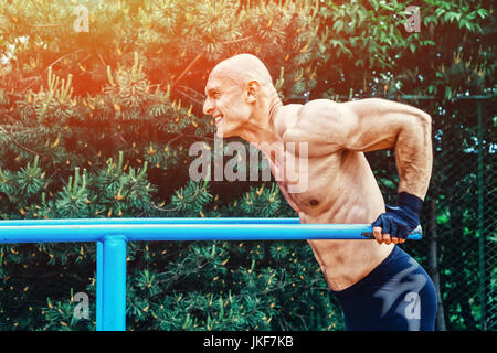 Glatze Mann tut Push Ups am Barren in einem Park Stockfoto