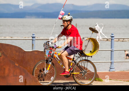 Morecambe, Lancashire, Großbritannien, Juli 2017. Pete Moser, ein Straßenunterhalter auf einem Fahrrad; One-man-Bands aus dem ganzen Land treffen sich auf der Morecambe Promenade zu einem lustigen, kostenlosen Festival des musikalischen Chaos. Die ein-Mann-Band hat einen besonderen Platz in der Fantasie aller, und diese Feier der Koordination ist ein einzigartiges Ereignis, das die Fantasie der Menschen anregt, unabhängig von ihrem Alter. Einmal gesehen, nie vergessen. Bands gibt es in allen Formen und Größen, die Musik aus jedem Genre wiedergeben. Stockfoto