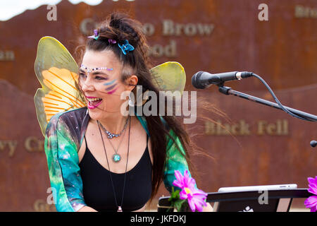 Serenity Sam von Cosmic Chords, singend mit Mikrofon. Im Juli treffen sich auf der Morecambe Promenade Multi-Instrument-One-man-Bands aus dem ganzen Land zu einem unterhaltsamen, kostenlosen Festival mit musikalischem Chaos. Diese ein-Frauen-Band hat einen besonderen Platz in der Phantasie aller und diese Feier der musikalischen Koordination ist ein einzigartiges Ereignis, das die Phantasie der Menschen, unabhängig von ihrem Alter, anzieht. Einmal gesehen nie vergessen. Bands gibt es in allen Formen und Größen, spielen Musik aus jedem Genre. Stockfoto