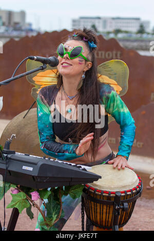 Serenity Sam von Cosmic Chords, singend mit Mikrofon. Im Juli treffen sich auf der Morecambe Promenade Multi-Instrument-One-man-Bands aus dem ganzen Land zu einem unterhaltsamen, kostenlosen Festival mit musikalischem Chaos. Diese ein-Frauen-Band hat einen besonderen Platz in der Phantasie aller und diese Feier der musikalischen Koordination ist ein einzigartiges Ereignis, das die Phantasie der Menschen, unabhängig von ihrem Alter, anzieht. Einmal gesehen nie vergessen. Bands gibt es in allen Formen und Größen, spielen Musik aus jedem Genre. Stockfoto