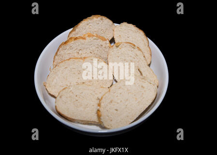 Sieben Scheiben knuspriges Brot auf einem weißen Teller und isoliert auf einem schwarzen Hintergrund. Stockfoto