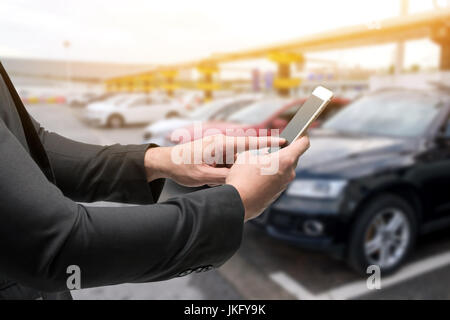 Car-sharing-Service oder Mietwagen Konzept. Austausch von Wirtschaft und kollaborativen Konsum. Kunde Mann Anzug Hand mit Smartphone mit Unschärfe Autos staatlich Stockfoto