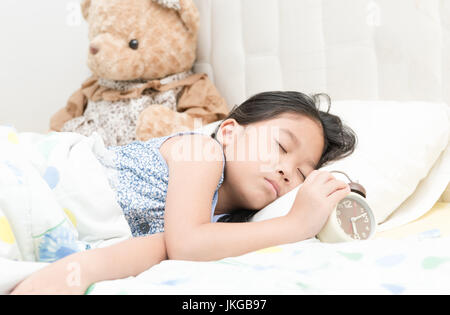 niedliche kleine Asiatin Schlaf und Touch Wecker am Bett im Schlafzimmer. Gesundes Konzept Stockfoto