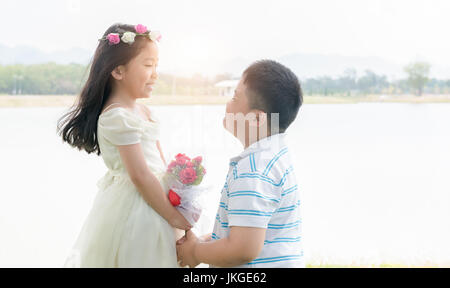 junge Bräutigam übergeben einen Strauß Rosen, der kleine Mädchen Braut auf See Hintergrund Stockfoto