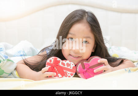 süße asiatische Mädchen Lächeln und lege mich auf dem Bett mit Valentinstag-Geschenk-Box. Stockfoto