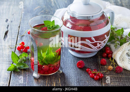 Früchte Beeren Tee mit Minze, roten Johannisbeeren und Himbeeren auf einem hölzernen Küchentisch. Stockfoto