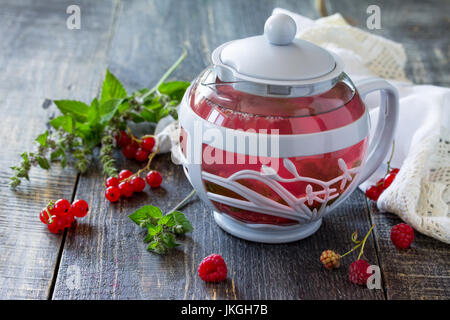 Früchte Beeren Tee mit Minze, roten Johannisbeeren und Himbeeren auf einem hölzernen Küchentisch. Stockfoto