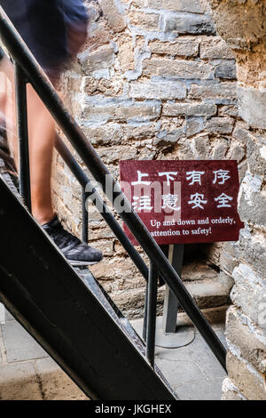 Menschen, die eine steile Treppe aus Metall, Chinesisch und Englisch sicher Warnschild am Ende Stockfoto