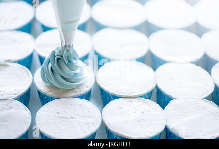Drücken Sie die Creme Füllung auf der blauen Cupcake, soft-Fokus Stockfoto