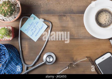 Papier Hinweis Patienten Termin am Holz Tafel mit Stethoskop, Krawatte, Smartphone, Gläser Kaffee und Kaktus auf Holz Hintergrund Stockfoto