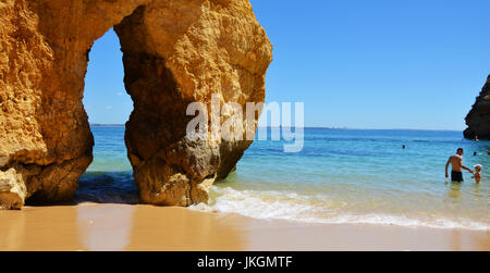 Berühmte Lücke zwischen Felsen an Camilo Strand (Praia Do Camilo) an der Algarve, Portugal mit türkisfarbenen Meer, Vater und Sohn im Hintergrund Stockfoto