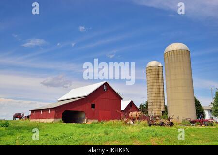 Eine rote Scheune und Silos sitzt unter Unordnung und verschiedene Gebäude auf einem Bauernhof in Lee, Illinois, USA. Stockfoto