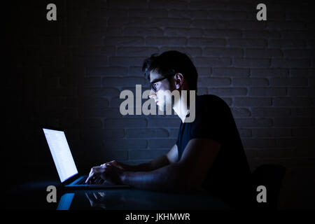 Junger Mann nachts im dunklen Büro am Computer arbeiten. Der Designer arbeitet in der späteren Zeit. . Hacker Stockfoto