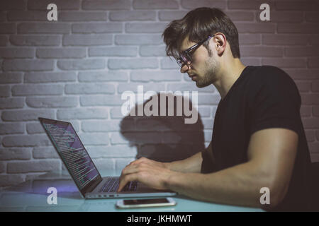 Junger Mann nachts im dunklen Büro am Computer arbeiten. Der Designer arbeitet in der späteren Zeit. . Hacker Stockfoto