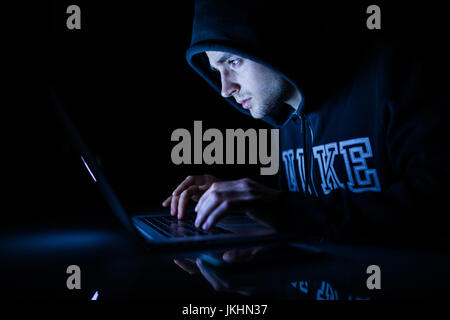 Der Mensch in eine Kapuze, die vor einem Laptop-Hacker knacken Programme in der Nacht arbeiten. Hacker Stockfoto