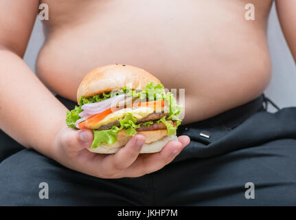 Hausgemachte Schweinefleisch Käse Hamburger in fettleibige Dicke hand auf grauem Hintergrund, Konzept Junk-Food und Ernährung Stockfoto