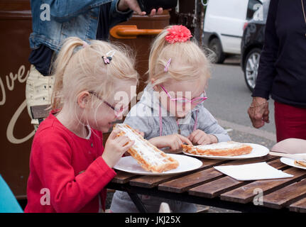 Zwei junge blonde Schwestern/Zwillinge essen Waffeln in einem Straßencafé Stockfoto