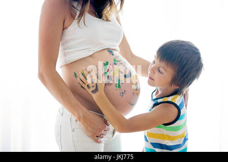 Glückliches Kind, junge, Malerei auf Mamas Bauch mit Farbe, isoliert auf weiss Stockfoto