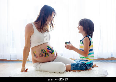 Glückliches Kind, junge, Malerei auf Mamas Bauch mit Farbe, isoliert auf weiss Stockfoto