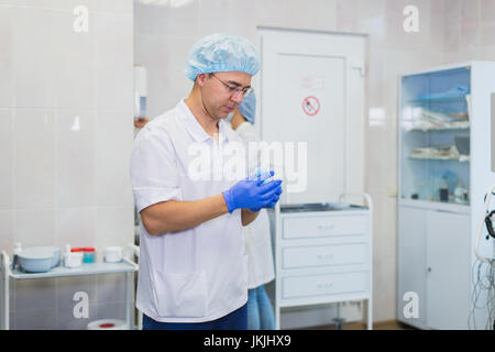 Schöne Reife Chirurg in blau medizinische Verschleiß und Maske setzt auf medizinische Handschuhe im OP-Saal Stockfoto