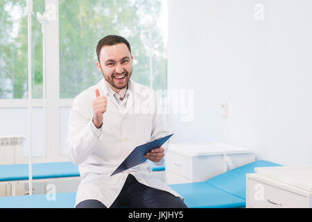 Fröhliche junge Ärztin hält ein Klemmbrett und Gestikulieren mit seiner Hand auf Krankenstation Stockfoto