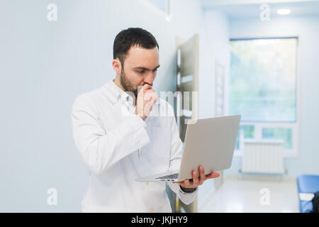 Erfolgreichen Arzt in seinem Büro stehen und Laptop für seine Arbeit mit Gleichgesinnten Stockfoto
