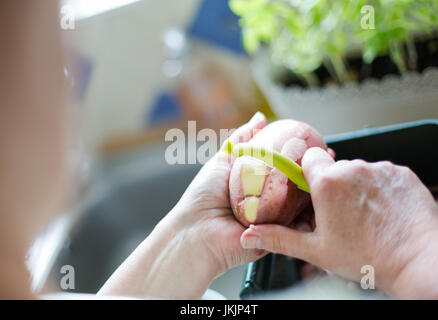 Ältere Frau rote Kartoffeln schälen Zubereitung von Speisen. Horizontale Ausrichtung mit selektiven Fokus auf Kartoffel und Schäler. Tageslicht Stockfoto