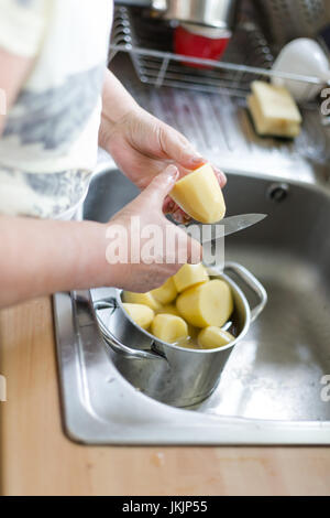 Ältere Frau schneidet geschälte Kartoffel, Zubereitung von Speisen. Vertikale Ausrichtung mit selektiven Fokus auf Kartoffel und Messer. Tageslicht Stockfoto